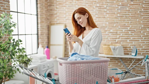 Çamaşırhanede Akıllı Telefon Kullanan Kendine Güvenen Genç Kızıl Saçlı Kadın — Stok fotoğraf
