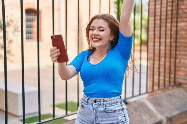 Νεαρή Κοκκινομάλλα Γυναίκα Χρησιμοποιώντας Smartphone Την Έκφραση Νικητής Στο Δρόμο — Φωτογραφία Αρχείου