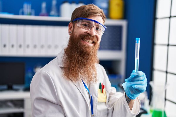 Young redhead man scientist smiling confident holding test tube at laboratory