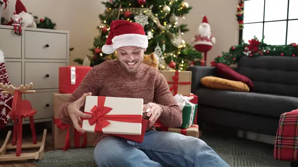 Νεαρός Καυκάσιος Άνδρας Ξεπακετάρει Δώρο Κάθεται Δίπλα Στο Χριστουγεννιάτικο Δέντρο — Φωτογραφία Αρχείου