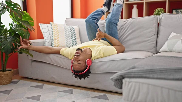 African american man listening to music lying on sofa playing air guitar at home