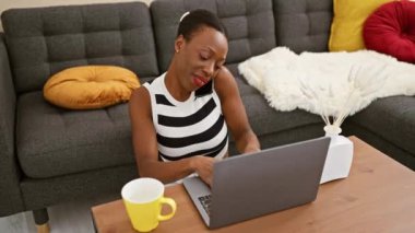 Güzel bir Afro-Amerikalı kadın ciddi bir online sohbete daldı. Evde dizüstü bilgisayar kullanırken telefonla konuştu. Kanepede oturdu, yanında kahve vardı.