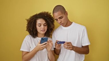 Akıllı telefon ve kredi kartı kullanan güzel bir çift izole edilmiş sarı arka planda.