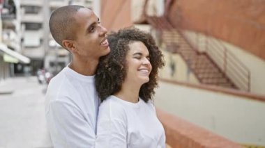 Güzel bir çift, kucaklaşıyorlar ve gülümsüyorlar, şehrin uğultulu caddesinde kendine güvenle gökyüzüne bakıyorlar. Aşk ve neşe dolu, bu mutlu anı dışarıda paylaşıyorlar, güneşin tadını çıkarıyorlar..