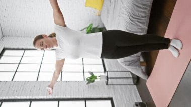 Güzel sarışın kadın dengeyi ve sakinliği bulur, yatak odasında durur, sabah yoga meditasyonuna odaklanır, spor kıyafetleri içinde dinlenir ve rahatlar..