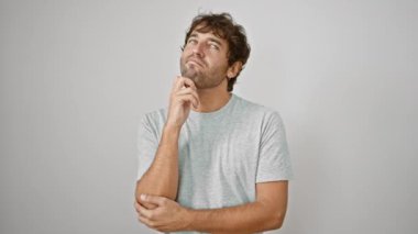 Tişörtlü düşünceli genç bir adam, eli çenesinde dinleniyor, dalgın bir gülümsemesi var. Şüphe denizinde, hileli bir soru üzerinde kafa yoruyor. Gıcır gıcır beyaz bir arkaplanda günlük, izole bir ekran görüntüsü.