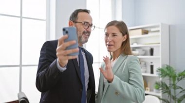Ofisteki akıllı telefondan görüntülü arama yapan iki iş adamı yan yana duruyor.