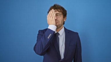 İş elbisesi içindeki genç adam gece geç saatlere kadar çalışmaktan yorgun, esniyor ve yüzünün yarısını mavi izole bir arka plan ile örtüyor, uykusuzluk ve yorgunluk yayıyor.