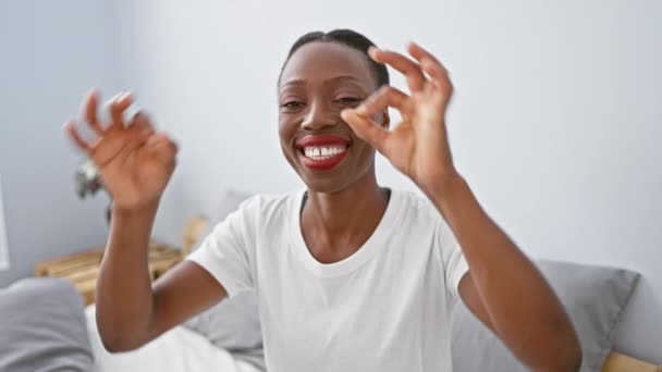 陽気なアフリカ系アメリカ人女性は ベッドの上に横たわり 自信を持って双眼鏡のように ジェスチャーをし 指を通して見ています ユーモラスな表情が部屋を満たしています — ストック動画