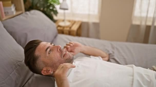 매력적인 히스패닉 남자는 편안하게 휴식을 취하고 머리에 침실에서 아늑한 침대에 — 비디오