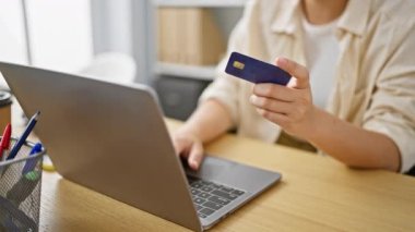 Gülümseyen genç İspanyol kadın, güzel bir iş adamı, ofisteki kredi kartı ve laptopunu kullanarak güvenli bir şekilde online finansmanda geziniyor..