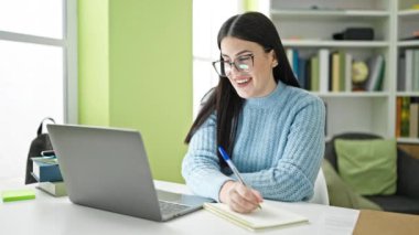 Genç kız dizüstü bilgisayarda çalışıyor ve notlar yazıyor.