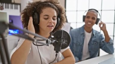 Şarkı söyleyen, dans eden ve müzik stüdyosunda mutlu mesut akustik müzik çalan kendinden emin müzisyenler, iki gülümseyen sanatçı - erkek ve kadın, mikrofonlara şarkı söylüyor, melodiler yaratıyor, kapalı alanda eğlence yaratıyor.