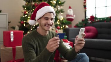 Mutlu genç adam Noel 'i cep telefonu, kredi kartı ve Noel Baba şapkasıyla kutluyor.