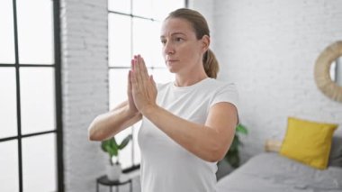 Uyanık ve dengeli, güzel, ciddi sarışın kadın yoga pozu veriyor, sabah egzersizi için yatakta duruyor, rahat yatak odasında sakin bir konsantrasyon yayıyor..