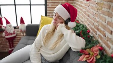 Noel şapkalı genç bir kadın oturma odasında kanepede oturmuş müzik dinliyor.