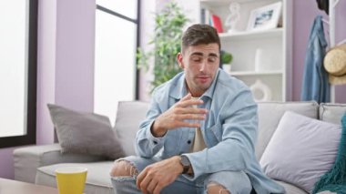 Yakışıklı, kendine güveni tam genç bir İspanyol sabah kahvesini içiyor, rahat evinde kanepede dinleniyor, yüksek sesle konuşuyor ve mutluluğunu paylaşıyor.