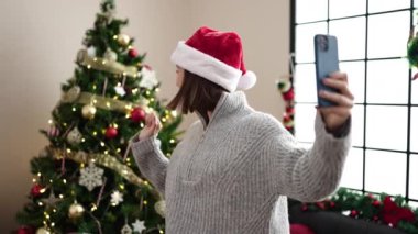 Akıllı telefonlu genç ve güzel bir İspanyol kadın. Kendine gülerek Noel ağacının yanında duruyor.