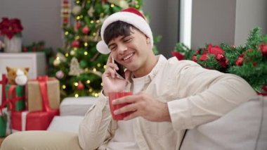 Noel Baba şapkalı genç adam evde Noel 'i kutluyor, cep telefonundan konuşuyor ve çay içiyor.