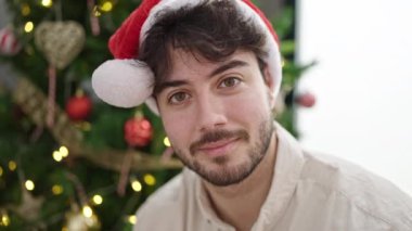 Arka planda Noel ağacı olan beyaz kazaklı genç bir adamın portresi. 