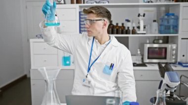 Laboratuvarda dizüstü bilgisayarla test tüpünde sıvı ölçümü yapan beyaz bir bilim adamı.