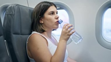 Kadın uçakta oturmuş su içiyor ve kameraya bakıyor. seyahat ve turizm kavramı.