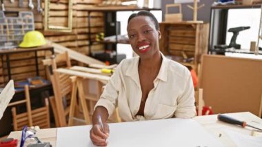 Güzel Afrikalı Amerikalı kadın marangoz gülümseyen ve usta marangozluk atölyesinde çizim yapan