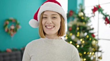 Evdeki Noel ağacının önünde gülümseyen genç sarışın kadın.