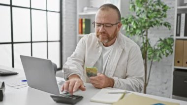 Yakışıklı yetişkin beyaz iş adamı Avustralya doları sayıyor, ofiste notlar alıyor. İşyerindeki başarılı orta yaşlı patronun gülümseyen portresi, servetinin tadını çıkarıyor..