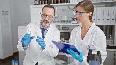 Laboratuvarlarının ortasında özenle çalışan laboratuvar önlüklü iki bilim adamı, değerli bir örneğin üzerine toplanmış, özenle not alıyorlar..
