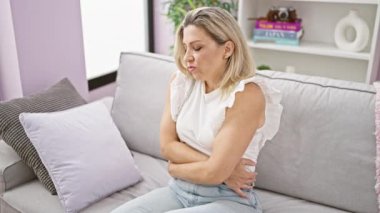 Genç sarışın kadın mide ağrısı çekiyor. Evdeki kanepede yatıyor.