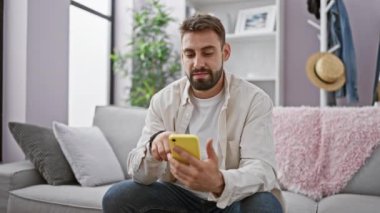 Young hispanic man using smartphone doing ok gesture at home