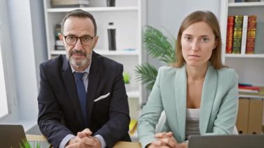İki ciddi yüzlü iş adamı bir projeye daldılar, ofis masasında birlikte oturuyorlar, bir dizüstü bilgisayar üzerinde çalışıyorlar, profesyonel başarıyı somutlaştırıyorlar.