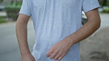 Rahat bir şekilde kendine güveni olan genç bir adam, şehir sokaklarında duruyor, kollarını kavuşturmuş bir jest yapıyor, dış şehrin arka planının altında yakın çekim yapıyor.