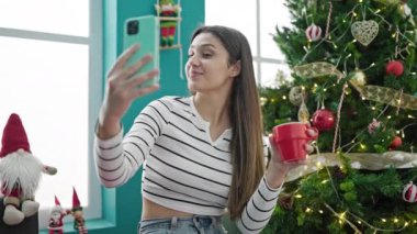 Mutlu genç kız sıcak içecek içiyor ve Noel 'i evde kutlarken cep telefonu kullanıyor.  