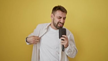 Neşeli, genç İspanyol bir adam, mikrofon olarak kendine güvenen, sarı arka planda izole edilmiş bir şarkıyla kalbini dışarı vuruyor.