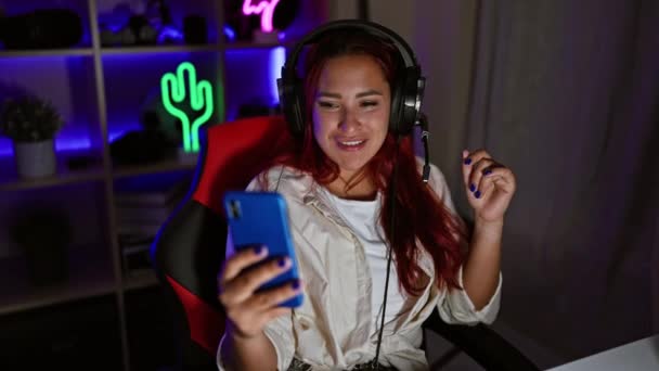笑顔の若い赤毛の女性ストリーマーゲームルームで屋内ビデオ通話を楽しんで 未来的なバーチャルエンターテイメントに完全に魅了 — ストック動画