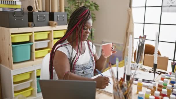 美しいアフリカ系アメリカ人女性アーティストが肖像画を描き 居心地の良いアートスタジオで朝のコーヒーを楽しく飲んでいます — ストック動画