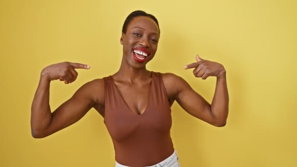 魅力的なアフリカ系アメリカ人女性は自信を持って指のジェスチャーで自分に向かって指を向ける 誇らしげにポーズし 黄色い孤立した背景に満足しています 彼女の輝く笑顔を撮影する美しい肖像画 — ストック動画