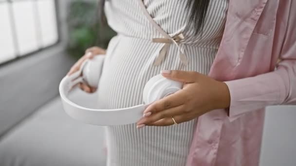 Erwartete Junge Hispanische Frau Setzt Kopfhörer Auf Babybauch Drinnen Entspannt — Stockvideo