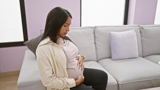 快乐的年轻孕妇漫不经心地坐在家里的沙发上 一边笑一边摸着肚子 把母亲抱在屋里 — 图库视频影像