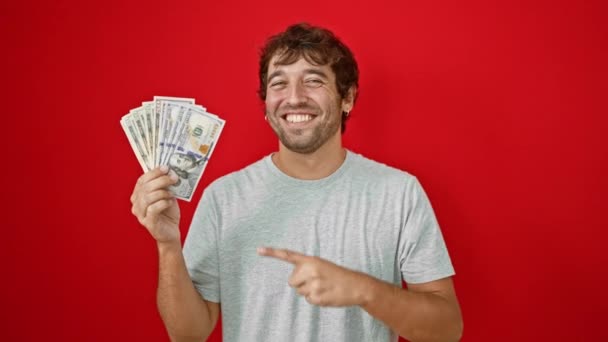 ひげのある陽気な若いブロンドの男は 自信を持って私たちアメリカの紙幣を指し示し 彼の赤い 孤立した背景に希望的な笑顔で — ストック動画