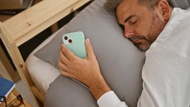 Utmattad Ung Latinamerikansk Gråhårig Man Bekvämt Sova Håller Smartphone Mysiga — Stockvideo