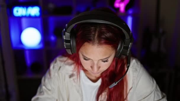暗い部屋でグリップゲームストリームに没頭し 深刻な顔 ヘッドフォンをスポーツし 仮想エンターテイメントの技術的に高度な領域で失われた若い赤毛の女性ストリーマー — ストック動画