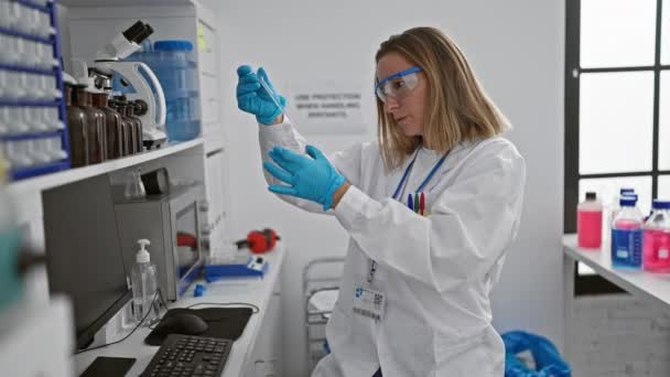 漂亮的金发女科学家在实验室里专心致志地从事批判性的医学研究 一边拿着试管一边在显微镜下专心工作 — 图库视频影像