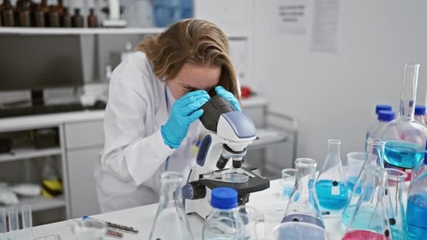 年轻的金发碧眼的女科学家在熙熙攘攘的实验室里 在显微镜下庆祝她取得的突破性的生物技术胜利 — 图库视频影像