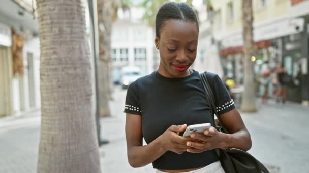 거리에 서있는 그녀의 전화에 행복하게 메시지를 보내는 즐거운 아프리카계 미국인 — 비디오