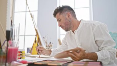 Genç, yakışıklı İspanyol bir adam hevesle kağıda resim çiziyor, sanatına dalmış ve vızıldayan bir stüdyoda konsantre olmuş.