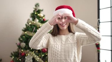 Noel Baba şapkalı güzel, mutlu genç bir kadın elleriyle kalp hareketi yapıyor.