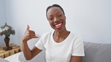 Neşeli Afro-Amerikan kadın yatakta yatıyor, eli ve parmaklarıyla bir telefon konuşması yapıyor. Çekici bir portre, rahatlatıcı yatak odasında neşeli bir yüz ifadesi yakalıyor.